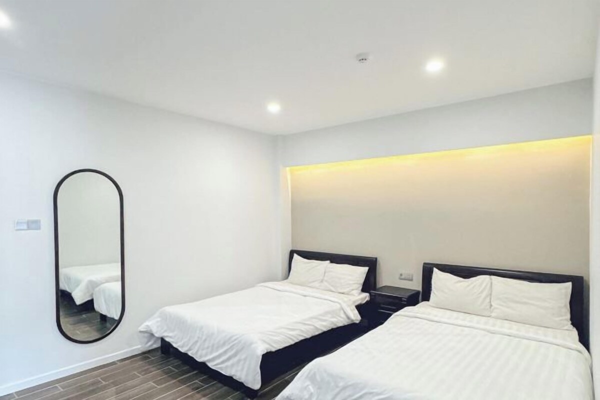 A modern hotel room with two single beds, a large mirror, and a wall-mounted light fixture.