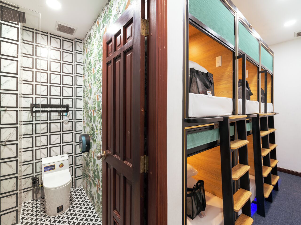 A hotel room with a shower area, a toilet, and a bunk bed with storage shelves.