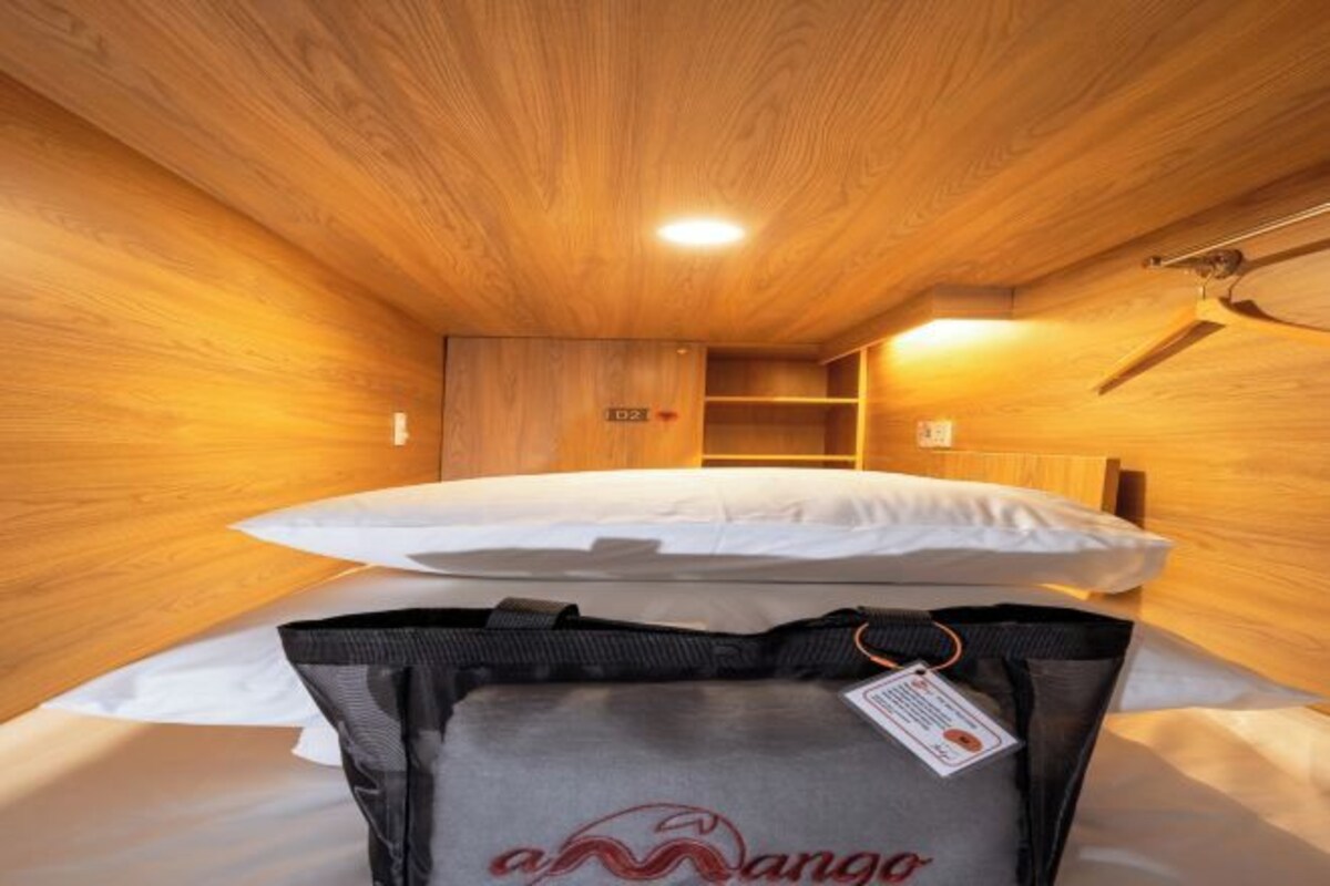 Ein Zimmer mit Holzwänden, einem Bett, einer kleinen Sitzecke und einem Koffer auf dem Boden.