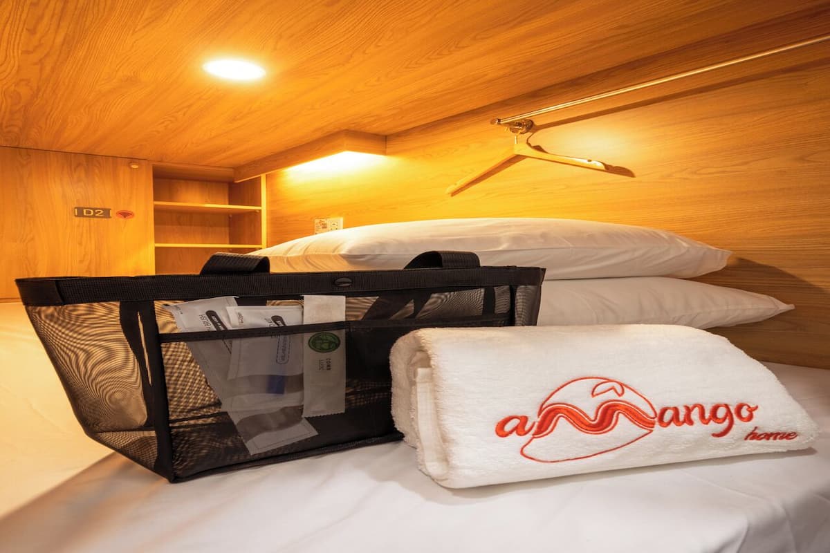 Una habitación de hotel con una cama, un cesto negro para guardar objetos y una toalla blanca con un logotipo.
