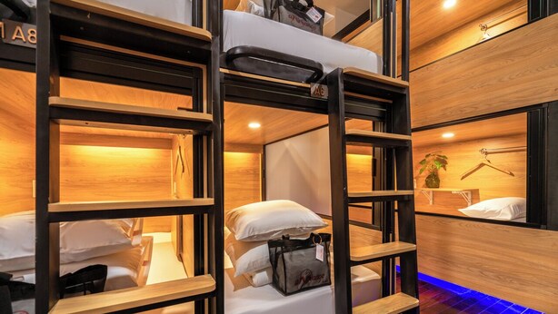 Dormitorio con literas de madera, una mesita de noche pequeña y una planta colgante.