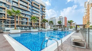 Een dakzwembad met een helderblauw wateroppervlak, omgeven door moderne gebouwen met balkons en palmbomen.