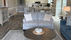 A spacious living room with a gray sofa, a coffee table, and a dining area with a chandelier. - Birdie on the Green in Myrtle wood (Myrtle Beach)