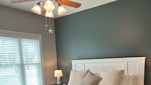 A bedroom with a bed, bedside tables, a ceiling fan, and a window with blinds. - Birdie on the Green in Myrtle wood (Myrtle Beach)