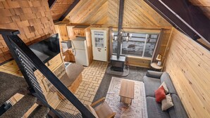 Ein gemütliches Blockhaus-Interieur mit Schlafgalerie, Kamin, einer Couch und einem Essbereich.
