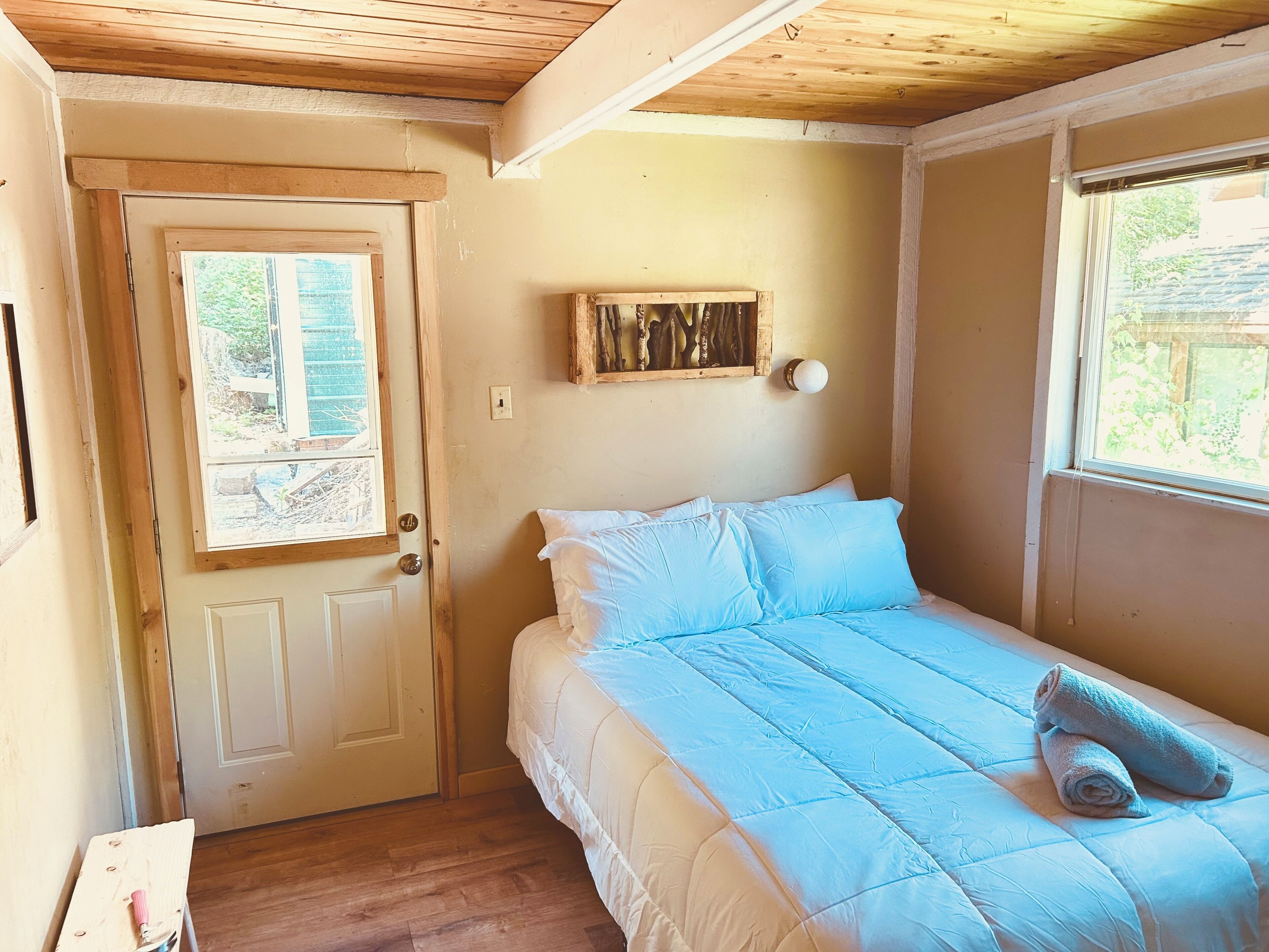 A bedroom with a bed, a door, a window, and a wall-mounted light fixture.