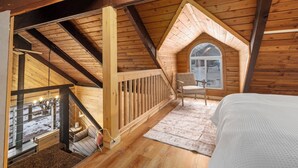 Ein gemütliches Schlafzimmer im Dachgeschoss mit Holzbalkendecke, kleinem Fenster, Bett und Stuhl.