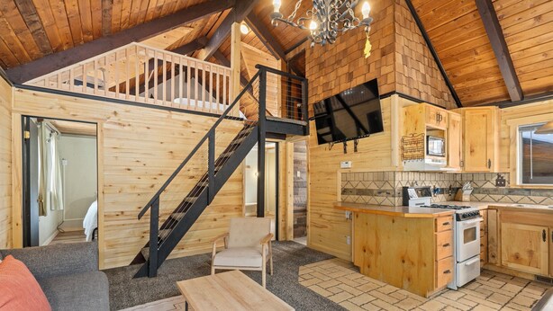 Ein großzügiger Loft-Raum mit einer Holztreppe, einer Küche mit eingebautem Ofen und einer gemütlichen Sitzecke mit Sofa und Tisch.