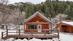 Eine Holzhütte mit Satteldach, einer hölzernen Veranda davor und einer Berglandschaft im Hintergrund.