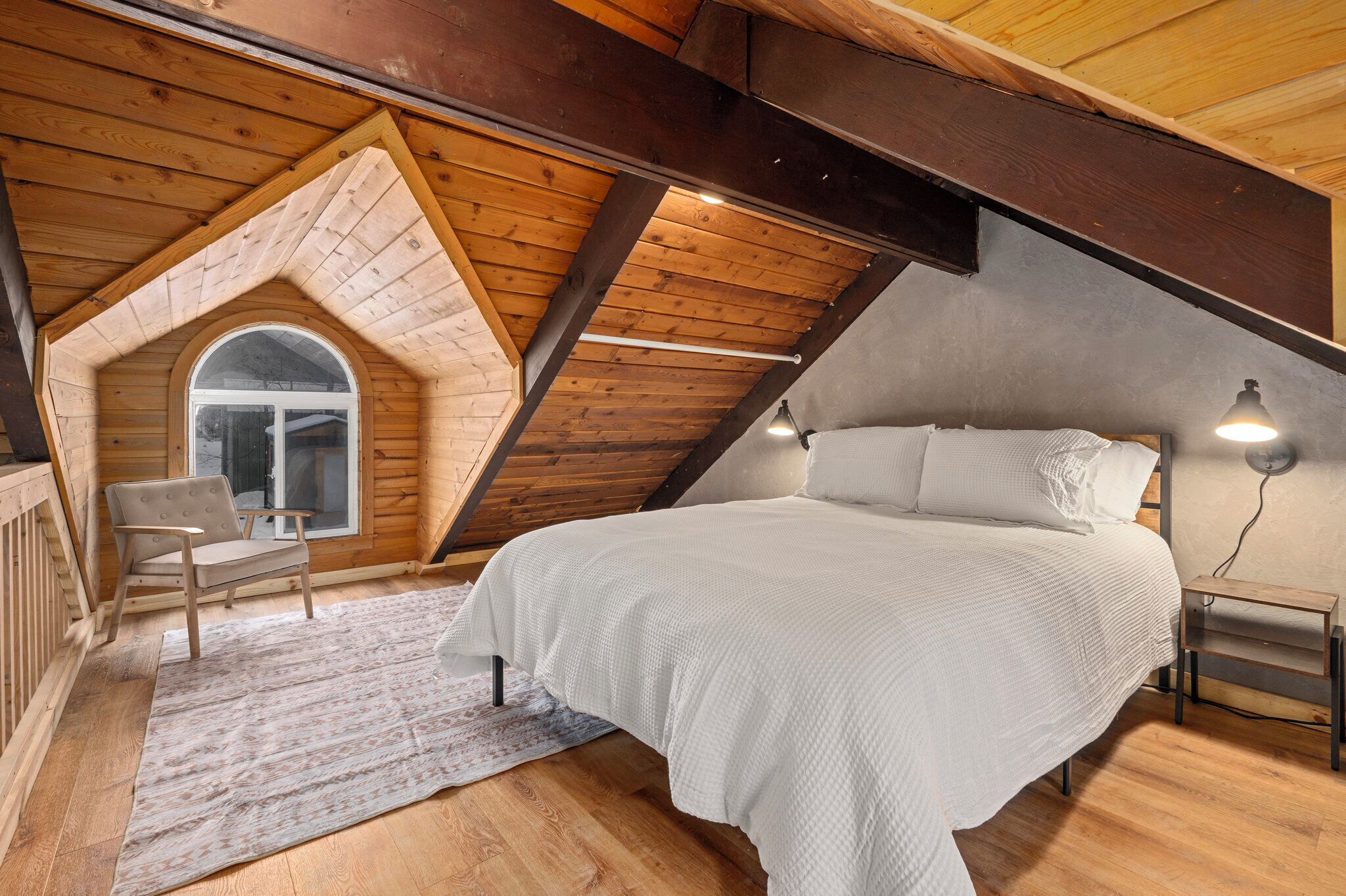 Ein gemütliches Schlafzimmer im Dachgeschoss mit schrägen Wänden, einem großen Bett, einem Sessel und einem kleinen Tisch.