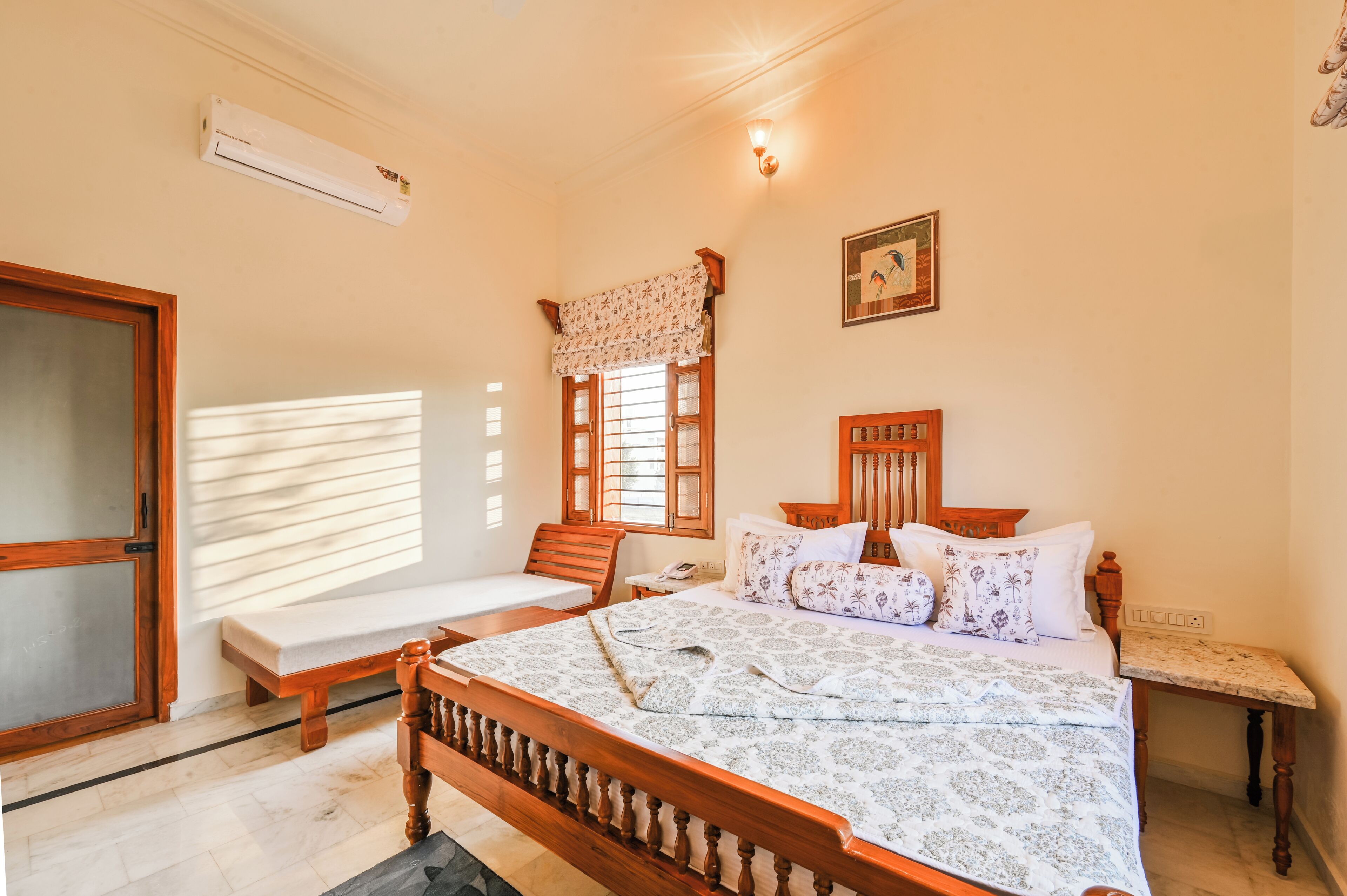A bedroom with a wooden bed, a bedside table, a nightstand, a window with blinds, and a wall-mounted air conditioner.