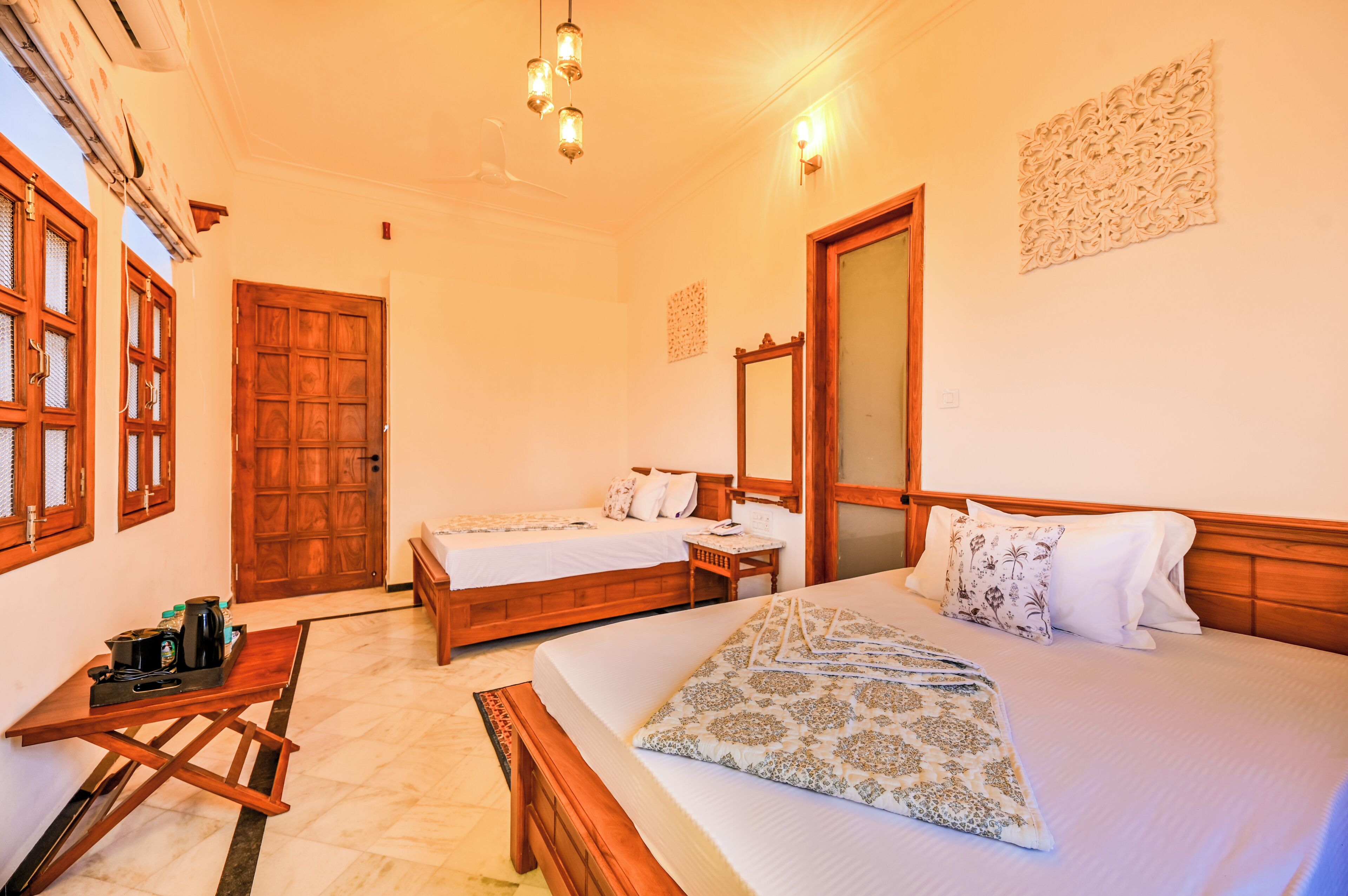 A hotel room with two beds, a wooden table with a tray, and a ceiling fan.