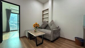 Ein Wohnzimmer mit grauem Sofa, einem kleinen Holztisch mit einer Vase voller Sonnenblumen und einem Balkon mit grauen Vorhängen.