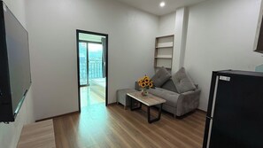 Ein modernes Wohnzimmer mit einem grauen Sofa, einem Couchtisch mit einer Vase voller Sonnenblumen, einem schwarzen Kühlschrank und einem Holzboden.