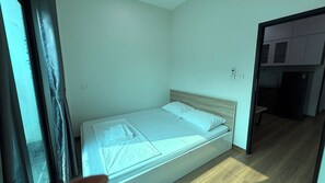 A small, single-bed room with a wooden headboard, a bedside table, and a window with curtains. - Era Apartment Doan Ke Thien  (Hanoi)