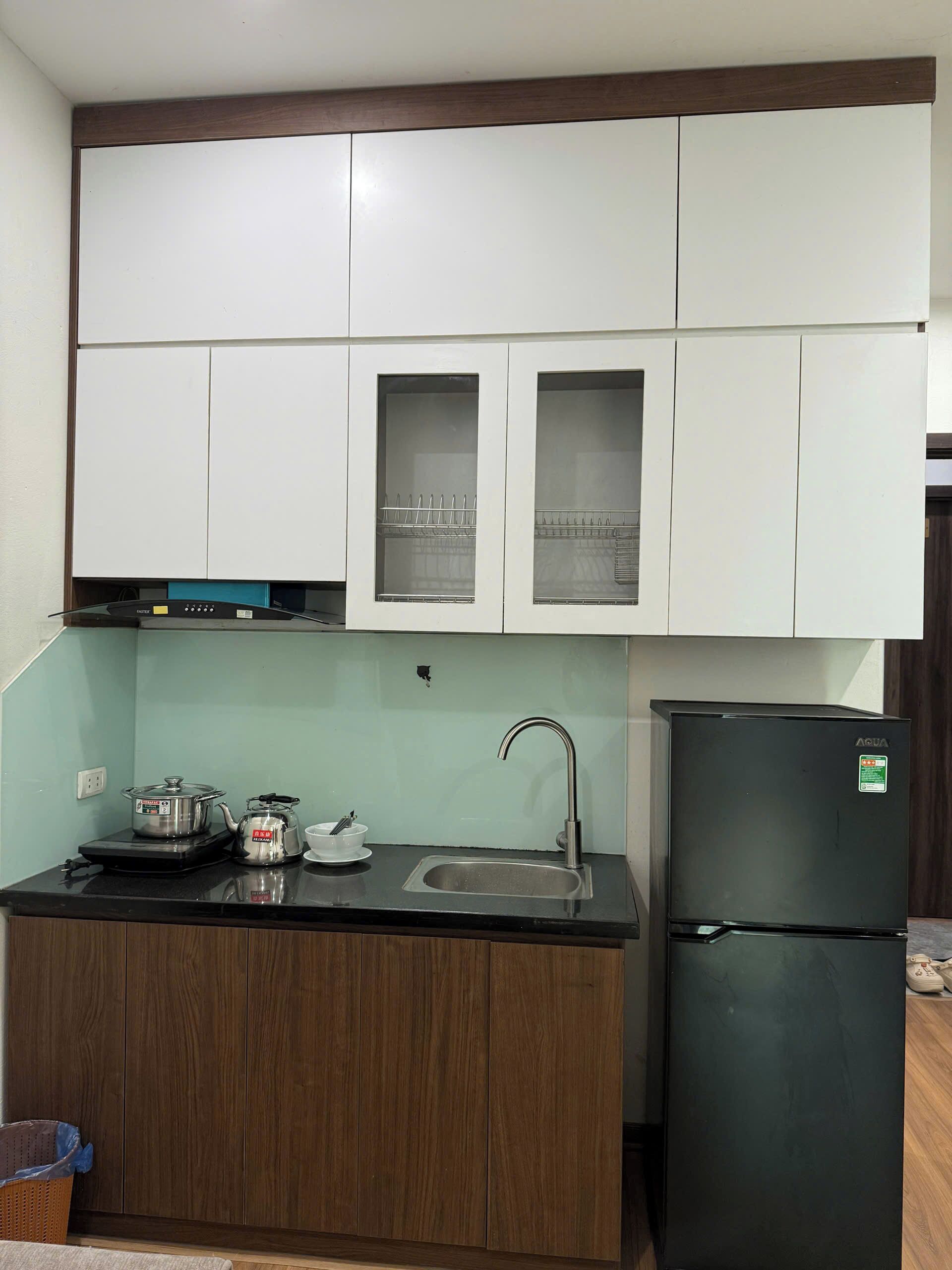Una cucina compatta con mobili bianchi, un piano di lavoro nero, un lavello in acciaio inossidabile, un frigorifero nero e un fornello.