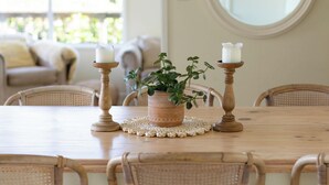 Ein Esstisch mit Korbstühlen, einem Blumentopf und Kerzen.