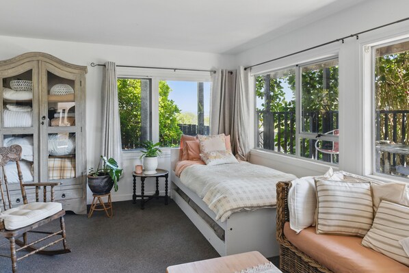 A cozy bedroom with a bed, a rocking chair, a small table with a plant, and a cabinet with storage. - The Sunshine House 🌞 Spacious & family friendly! 2 houses in 1! (Russell)
