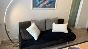Ein modernes Wohnzimmer mit einer schwarzen Couch, einem gerahmten abstrakten Gemälde und einer gebogenen Stehlampe.