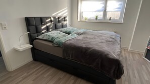 Un dormitorio moderno con una cama, una mesita de noche, una ventana con plantas y un radiador.