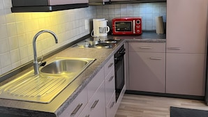 Eine moderne Küche mit grauen Schränken, einer Edelstahl-Spüle, einer roten Mikrowelle und einem eingebauten Backofen.