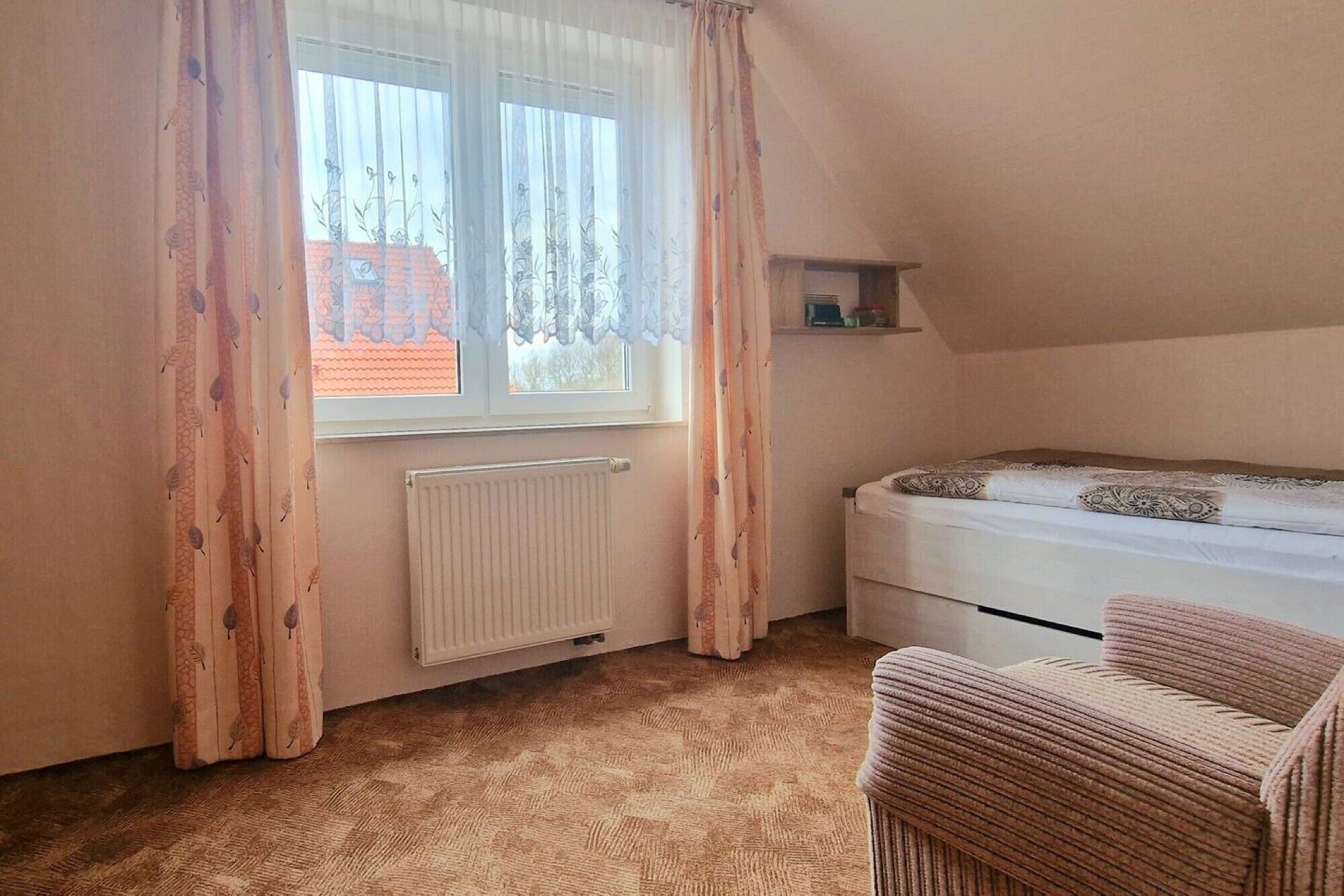 A bedroom with a bed, a radiator, a window with curtains, and a chair.