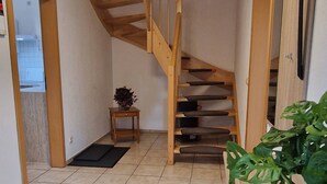 Un escalier avec des rampes en bois, une petite table avec une plante et un sol carrelé.