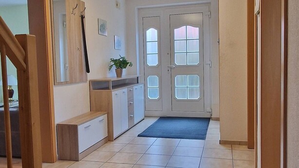 Un couloir avec un banc en bois, une plante en pot, une porte avec des panneaux de verre et un sol carrelé.