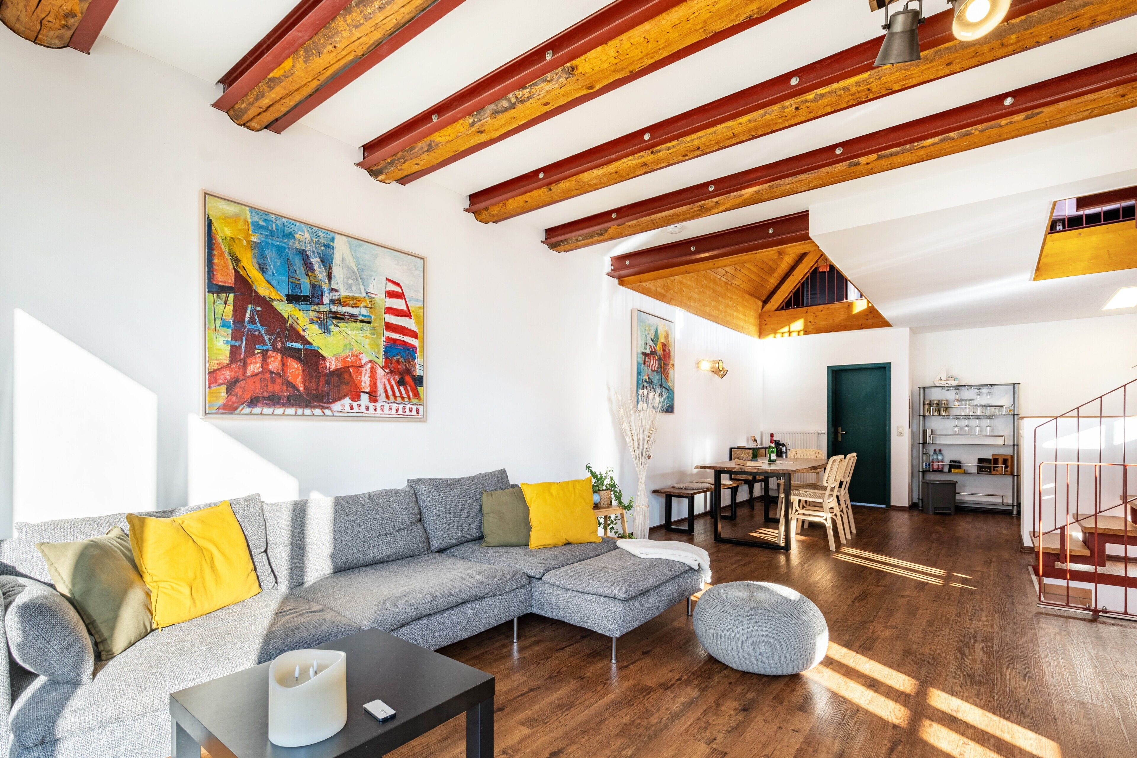 Una sala de estar moderna con un sofá seccional, vigas de madera, un comedor y obras de arte en las paredes.