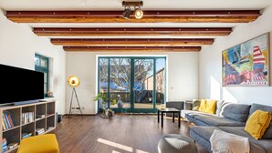 Ein Wohnzimmer mit Fernseher, Bücherregal, Sofa und einem großen Fenster.