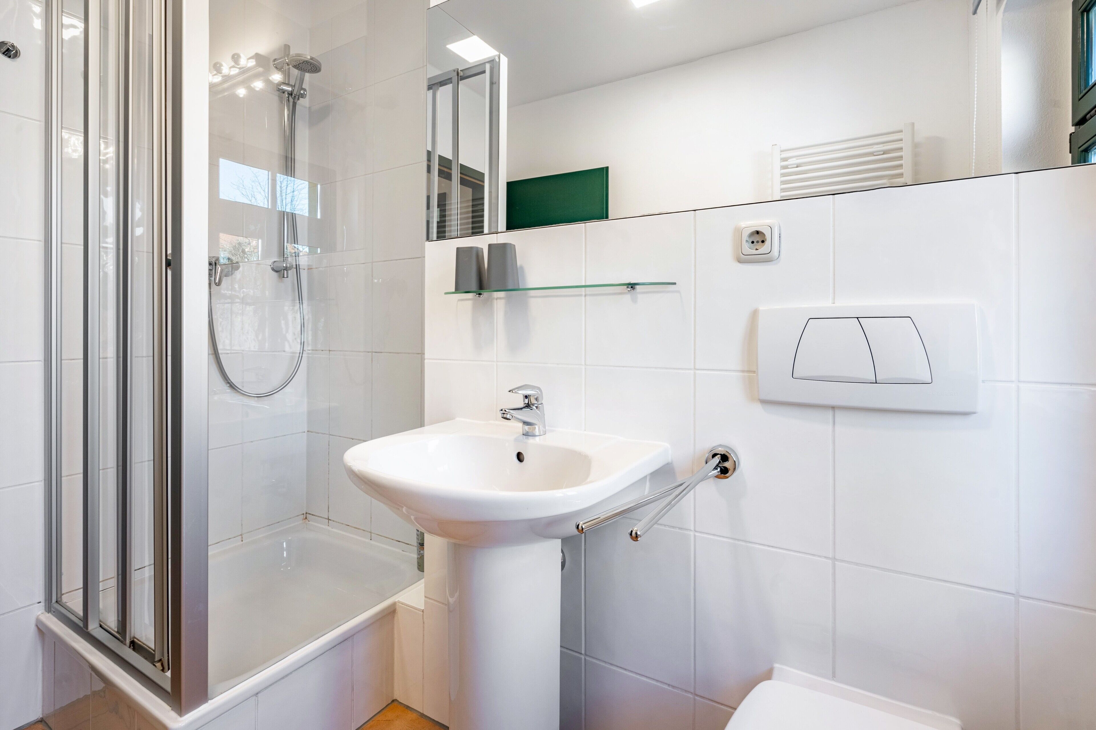 Ein modernes Badezimmer mit einer Duschkabine aus Glas, einem weißen Waschbecken und einem Spiegel.