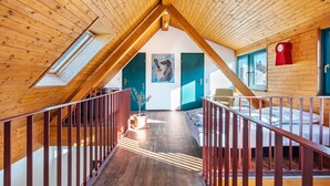 Ein Zimmer mit hohen Decken, Holzbalken, einem Oberlicht, einem Bett, einer roten Uhr und einem Gemälde an der Wand.