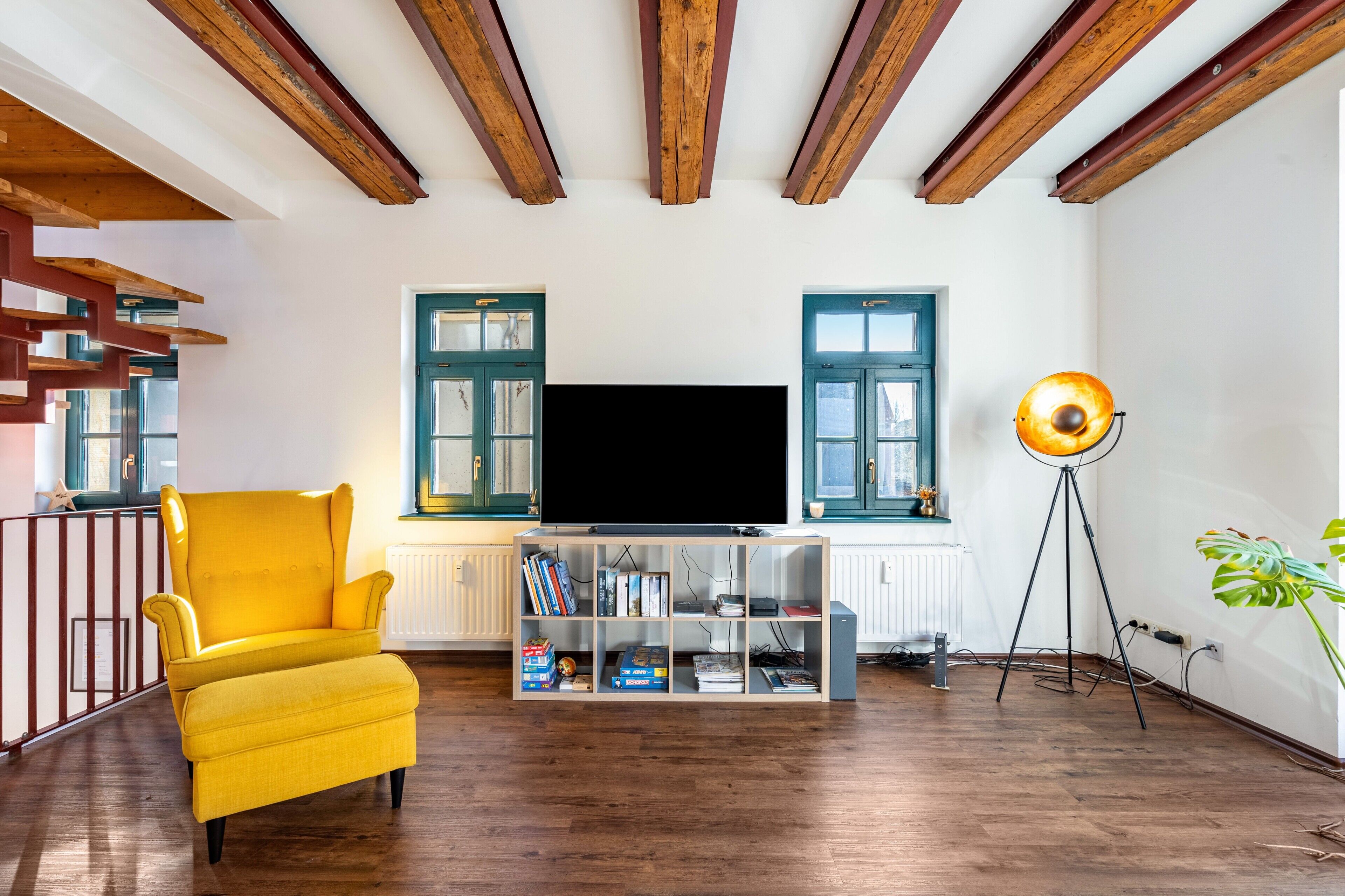 Ein Wohnzimmer mit einem gelben Sessel, einem Fernseher und einem Bücherregal.