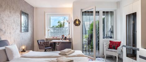 A modern hotel room with two beds, a desk, a chair, a balcony with a view, and a wardrobe.