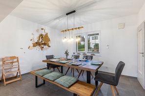 A dining area with a wooden table, chairs, a bench, and a hanging light fixture.