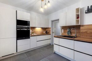 A modern kitchen with white cabinetry, a built-in oven, a wooden countertop, and a stainless steel sink. - Wellness & Playroom · Sauna, Whirlpool, Fireplace for Families in Winterberg (Winterberg)