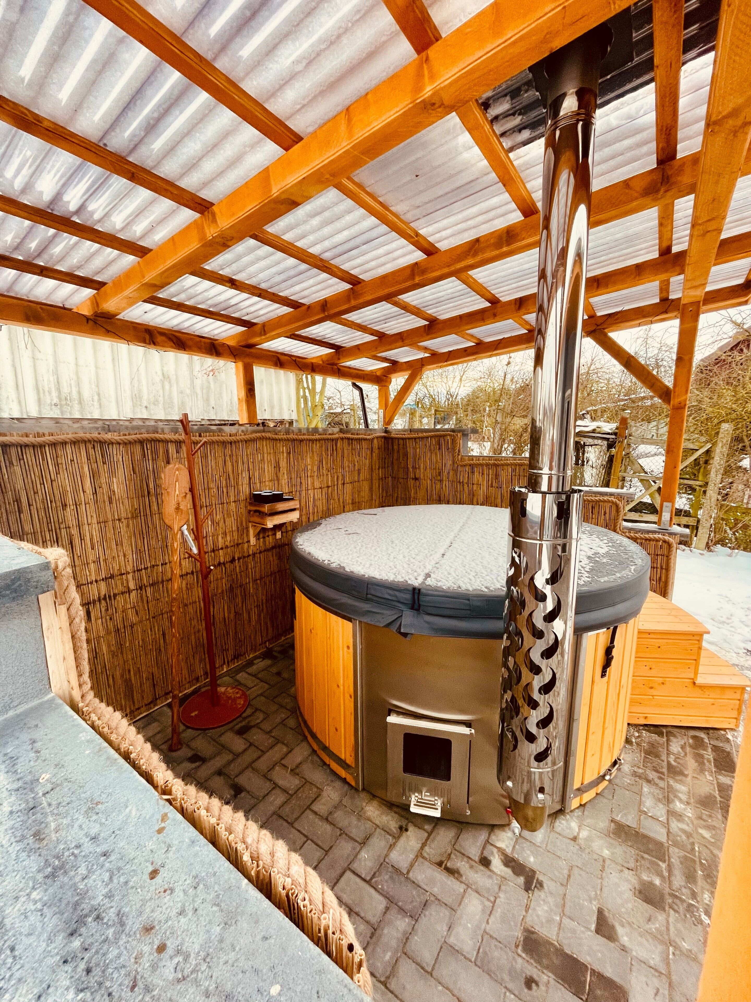 Ein Whirlpool mit Metallschornstein, Holzbalken und einer Bambuswand.