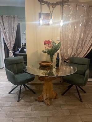 En matplats med ett glasbord, två grönklädda stolar, en trädstam som bordsfot, en vas med blommor och en kristallkrona.