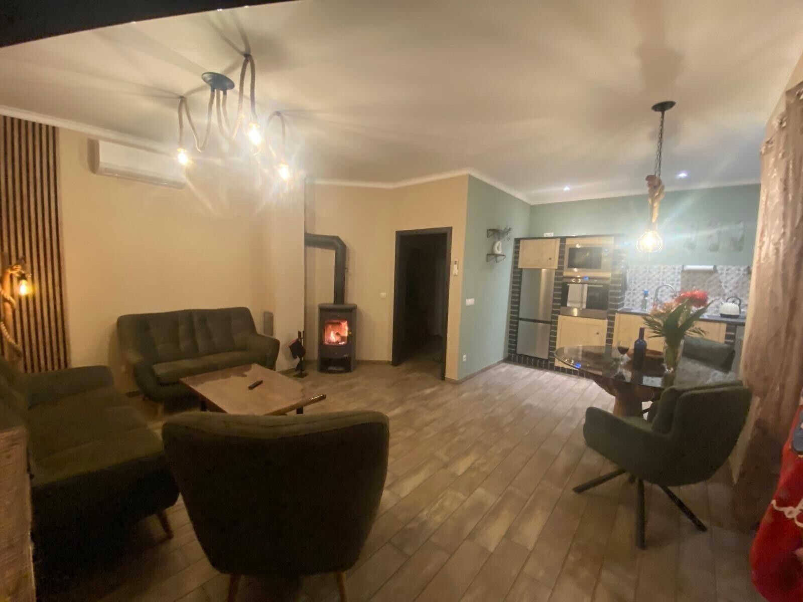 Een woonkamer met een bank, stoelen, een salontafel, een open haard en een keukenhoek met een koelkast en magnetron.