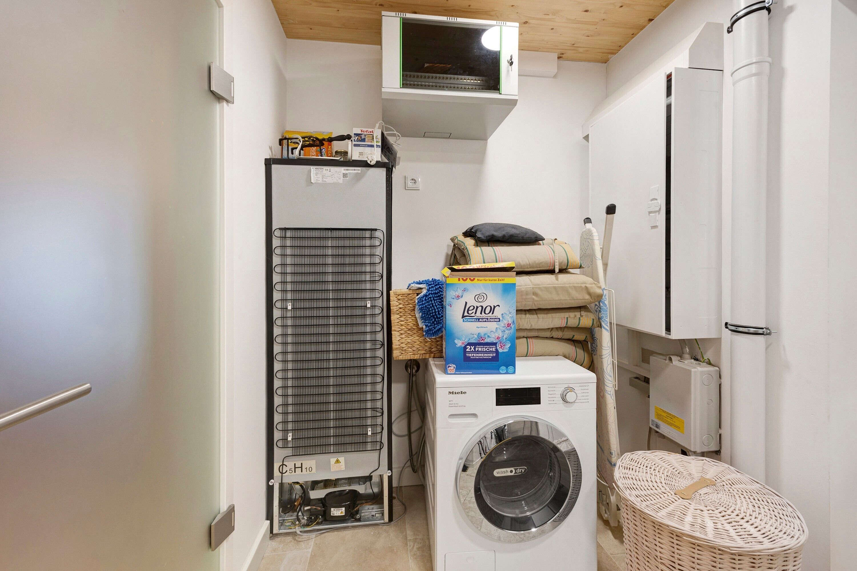 Une petite buanderie équipée d’un lave-linge, d’un sèche-linge, d’un radiateur et d’une petite étagère contenant des produits de nettoyage.