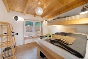 Una habitación con una cama, una escalera de madera, una lámpara colgante y un ventanal.