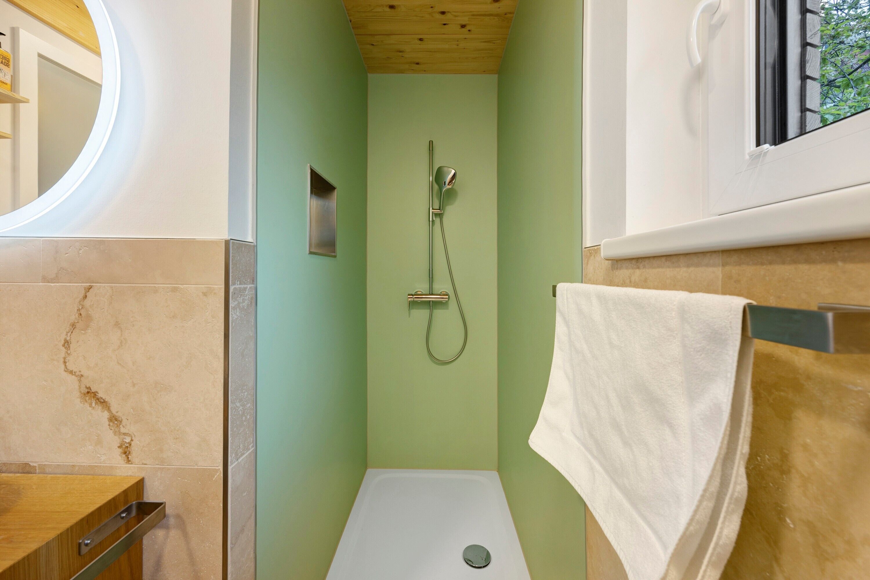 Un bagno doccia piccolo con soffitto in legno, un asciugamano bianco appeso a un portasciutto metallico e un piccolo ripiano.