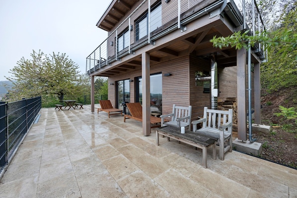 Una casa moderna con un porche cubierto, mobiliario exterior y vistas del paisaje circundante.