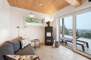 Ein modernes Wohnzimmer mit einer Couch, einem kleinen Tisch, einem Schrank und Blick ins Freie durch große Fenster.