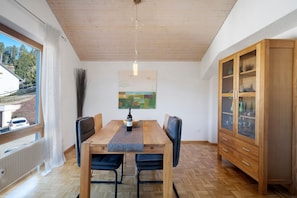 Een eethoek met een houten tafel, stoelen, een wijnfles en een kast.