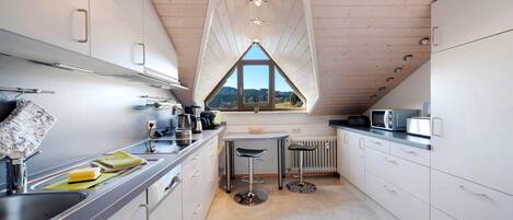 A modern kitchen with white cabinets, a central island, and a view through a triangular window.