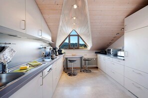 Een moderne keuken met witte kasten, een centraal eiland en uitzicht door een driehoekig raam.