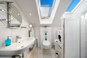 Une salle de bain moderne dotée d’une lucarne, d’un lavabo, de toilettes et d’un lave-linge.
