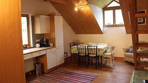 A cozy attic bedroom with a sloped ceiling, a dining table with chairs, and a small sofa.