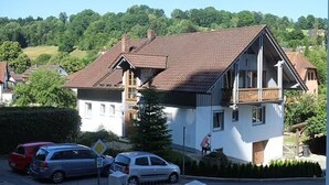 A two-story house with a sloped roof, a balcony, and a driveway with parked cars.